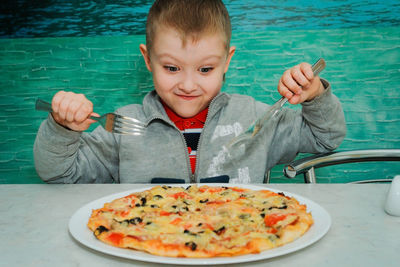 Cute boy looking at pizza in plate at table