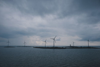 Windmills at beach against cloudy sky