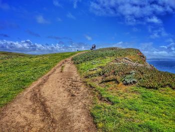 Dirt road amidst land against sky