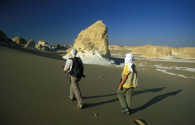 Rear view of men walking on desert landscape