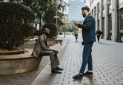 Businessman discussing with male colleague on footpath in city