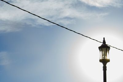 Low angle view of lamp post and cable against sky on sunny day