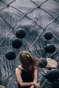 Woman with tousled hair sitting against black balloons