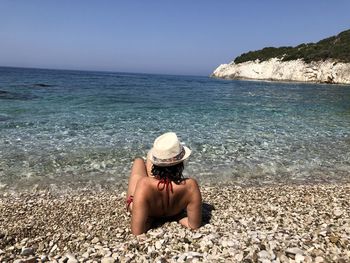 Rear view of woman relaxing at beach against sky