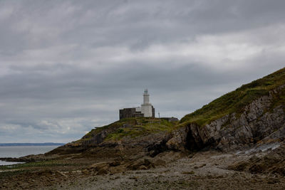 Lighthouse amidst buildings against cloudy sky
