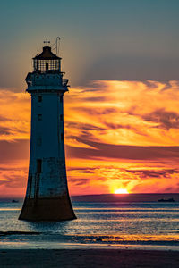 Lighthouse by sea against sky during sunset