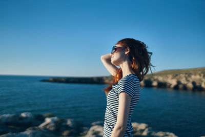 Woman standing against sea against clear blue sky