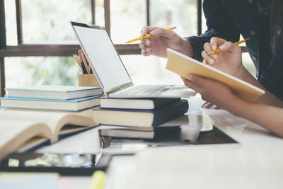 Cropped image of students using laptop while studying on table