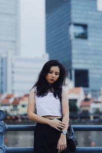 Thoughtful young woman standing against buildings in city