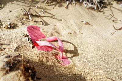 A single pink flip-flop shoe lies deserted on a sandy beach, it is partially covered with sand