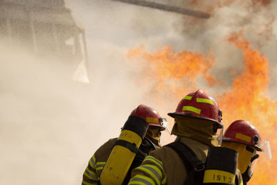 Firefighters standing against fire 