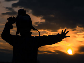Silhouette man with woman standing against orange sky