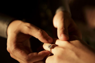 Cropped hands of man putting ring in woman finger at home