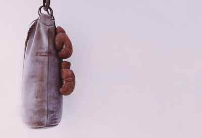 Punching bag hanging with boxing gloves by white wall
