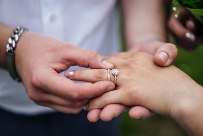 Midsection of man putting ring in woman finger outdoors