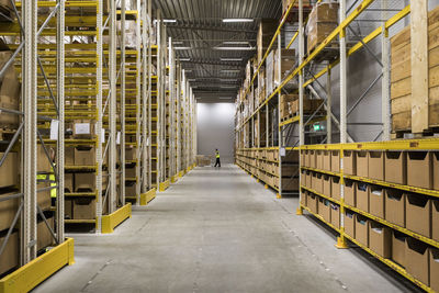 Aisle amidst packages on racks at illuminated distribution warehouse