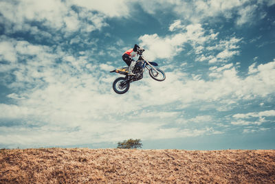 Low angle view of man jumping while riding motorcycle against sky