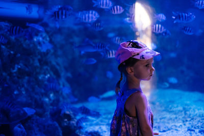 Child is looking at fishes in oceanarium. toddler girl enjoying underwater life in big aquarium in