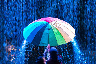 Rear view of children holding umbrella under rain during night