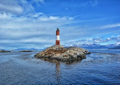 Lighthouse amidst sea and buildings against sky