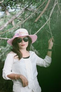 Portrait of young woman wearing sunglasses standing against plants