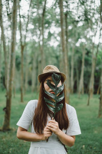 Young woman holding leaves while standing in forest