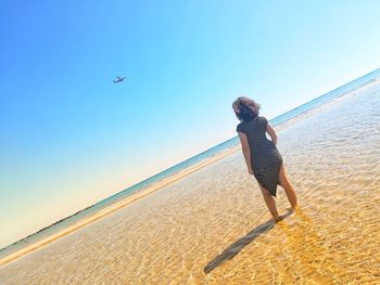 Woman standing on beach against clear sky