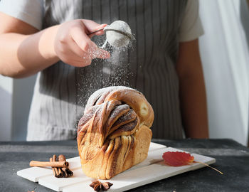 Teenager girl powdering pull apart cinnamon swirl bread with sugar. traditional sweet loaf 