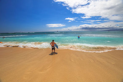 Rear view of man with surfboard on shore at beach against sky