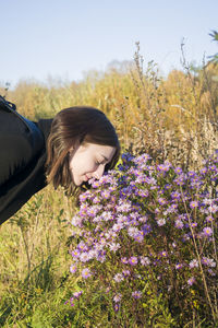 Woman smelling flowering plants on field