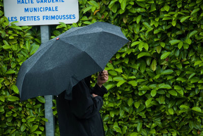 Man carrying umbrella standing against signboard and plants