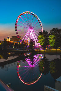 Ferris wheel by illuminated city against sky at night