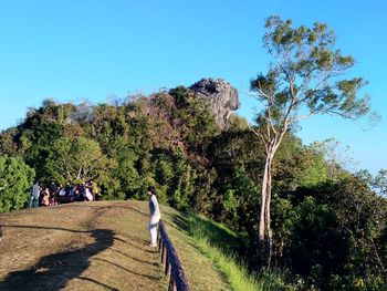 Rear view of people walking on landscape against clear blue sky