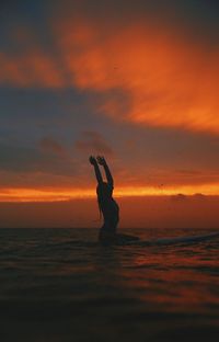 Silhouette woman in sea against sky during sunset