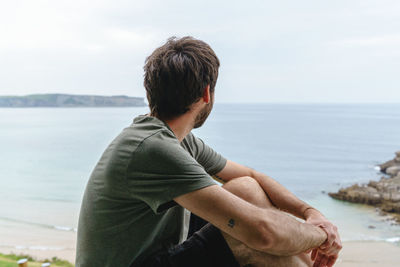 Side view of young man looking at sea against sky