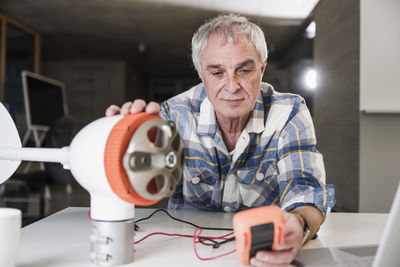 Engineer checking current of wind turbine rotor using multimeter at office