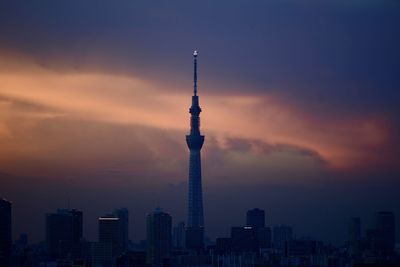 Communications tower in city against romantic sky at sunset