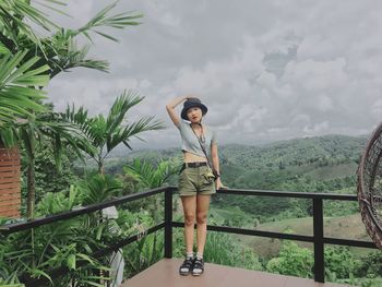 Young woman standing by railing against trees