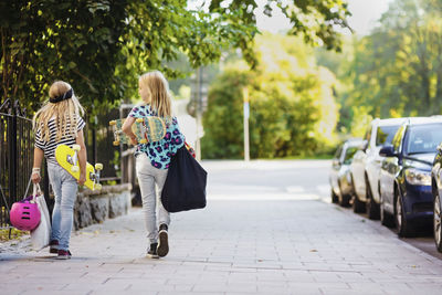 Rear view of girls with skateboards walking on cobbled street