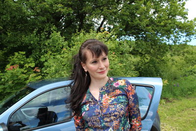 Woman looking away while standing by car on field