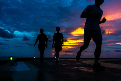 Silhouette people standing on beach against sky during sunset