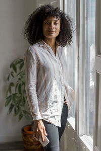 Confident female entrepreneur with smart phone standing near window in office