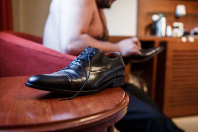 Close-up of shoe on table against shirtless man sitting on sofa