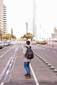 Rear view of a young teen with backpack skateboarding in city street