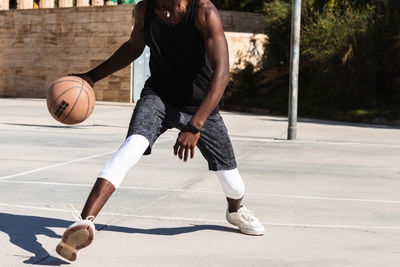 Cropped unrecognizable african american male athlete playing basketball on court in summer and looking at camera