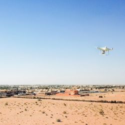 Airplane flying over sand against clear blue sky