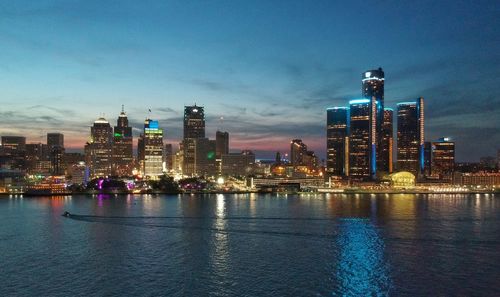 Illuminated buildings by river against sky in city