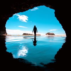 Silhouette woman standing with reflection in cave against sky