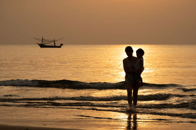 Silhouette mother carrying son while standing in sea during sunset