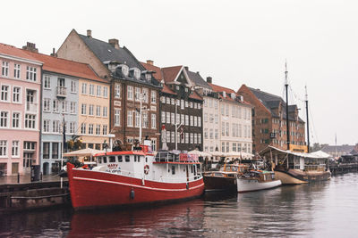 Sailboats moored on river by buildings against sky